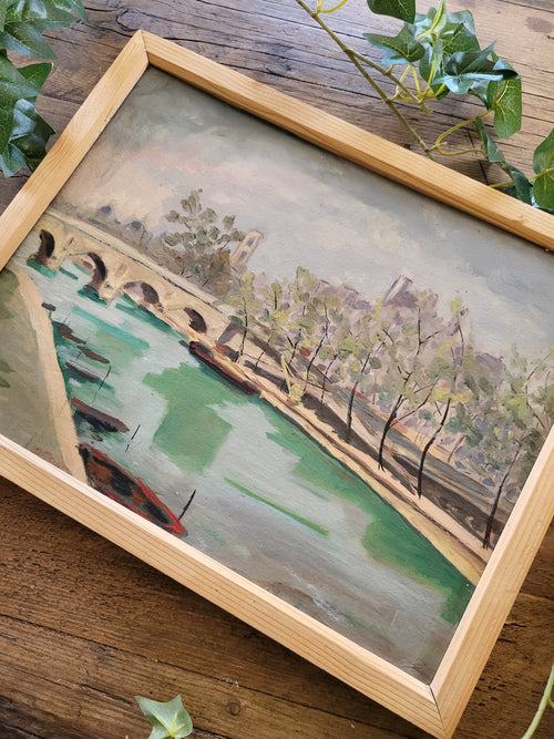 Framed painting of a landscape with trees and a building on a wooden surface.